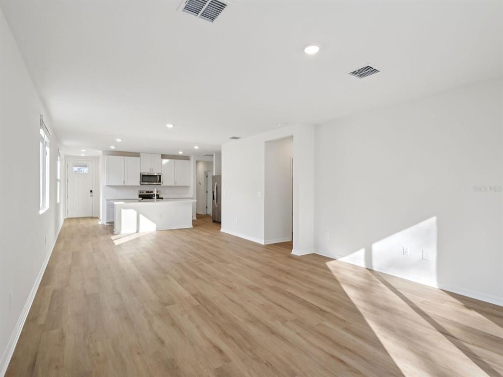 An open-concept living area features light wood-look flooring, white walls, and a kitchen with white cabinetry — 3474 MOSCATO DRIVE, BROOKSVILLE, FL