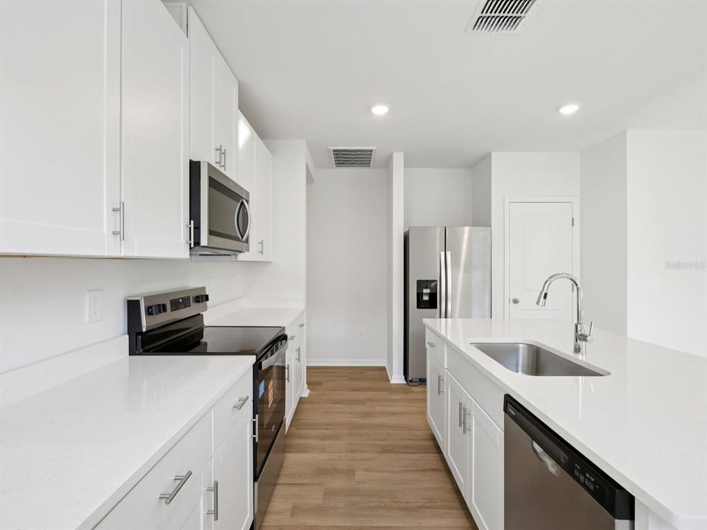 A modern kitchen features white cabinets, quartz countertops, stainless steel appliances, and wood-look flooring — 3474 MOSCATO DRIVE, BROOKSVILLE, FL