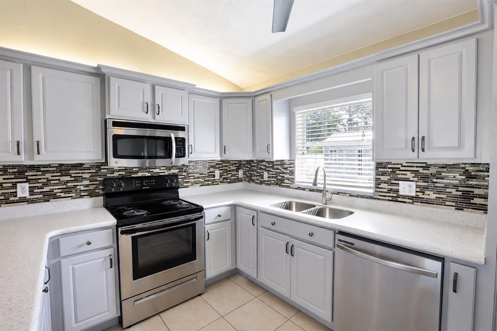 A kitchen with white cabinets, stainless steel appliances, white countertops, and a mosaic tile backsplash — 4 SEVERN COURT, PALM COAST, FL