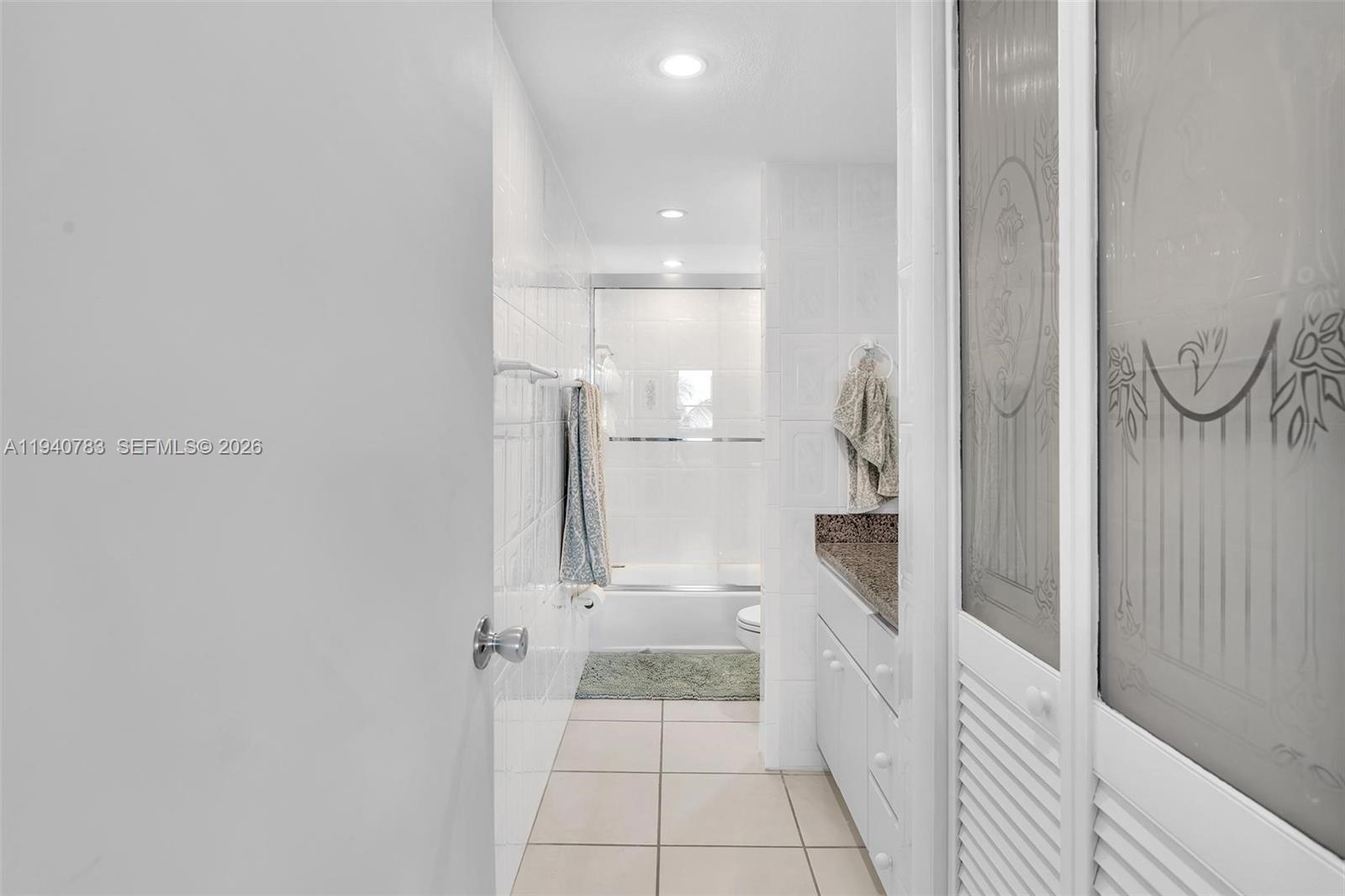 A bathroom features white tiled walls, a vanity with a granite countertop, and a shower — 5005 Collins Ave # 824, Miami Beach FL 33140, MIAMI BEACH, FL