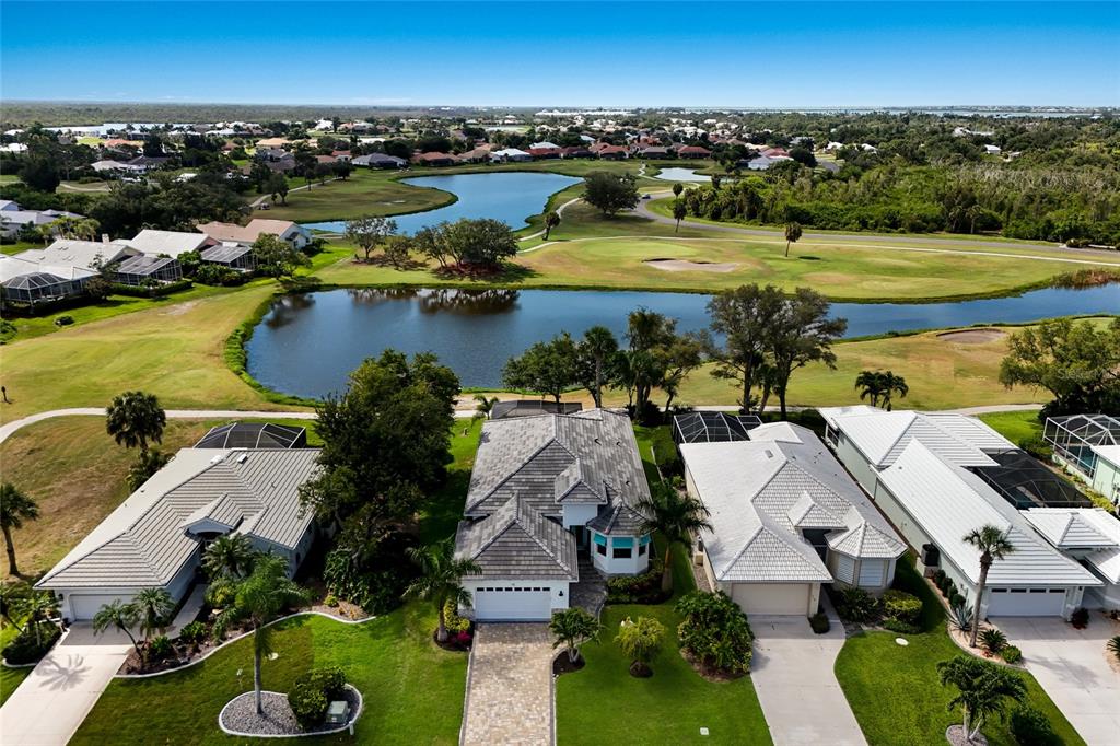 An aerial view shows three houses with tiled roofs situated along a golf course pond — 115 WESTWIND DRIVE, PLACIDA, FL