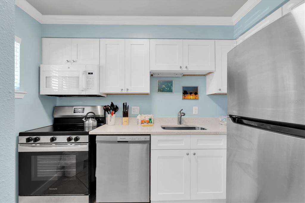 A kitchen features white cabinets, stainless steel appliances, and light blue walls — 19417 GULF BOULEVARD UNIT E103, INDIAN ROCKS BEACH, FL