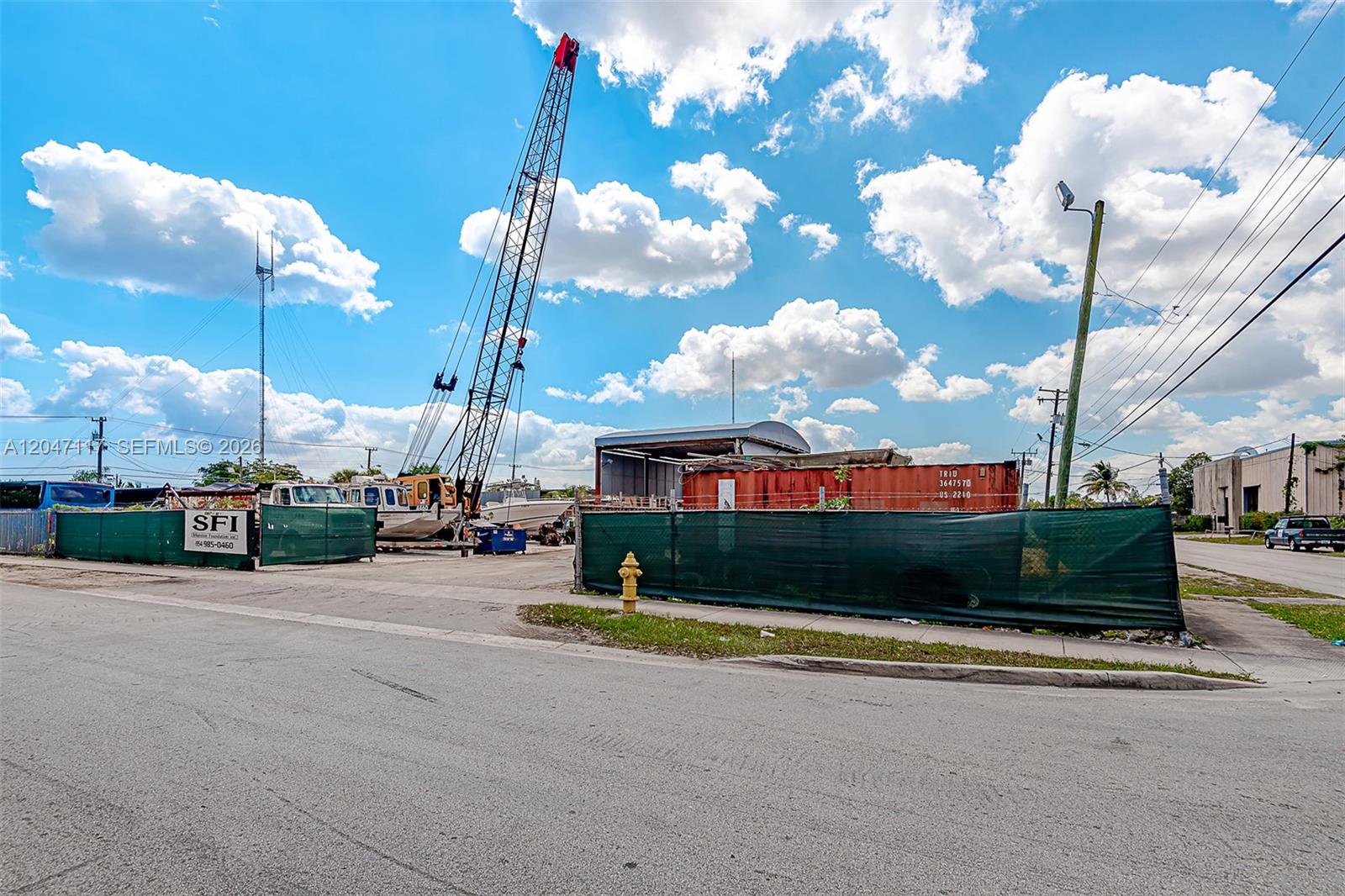 An outdoor construction or storage lot features a crane, shipping container, and green privacy fencing — 2301 SW 57th Ave, West Park FL 33023, WEST PARK, FL