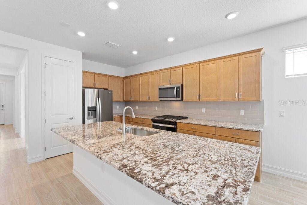 A kitchen features light wood cabinets, granite countertops, a large island, and stainless steel appliances — 3320 NW 52ND AVENUE ROAD, OCALA, FL