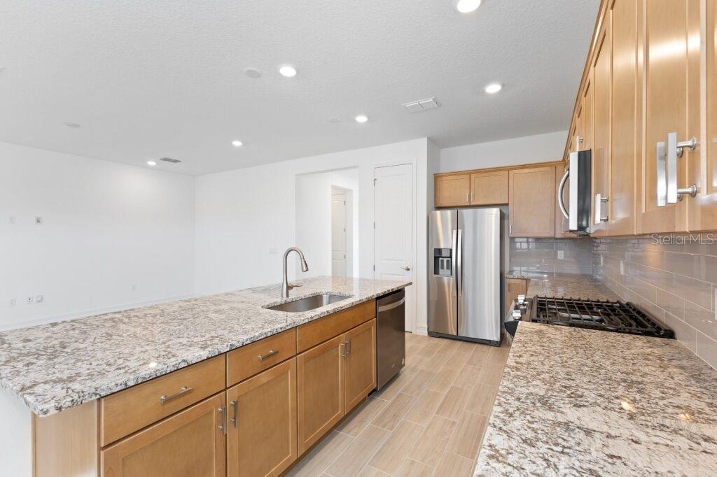 A kitchen features light wood cabinets, granite countertops, a center island, and stainless steel appliances — 3320 NW 52ND AVENUE ROAD, OCALA, FL