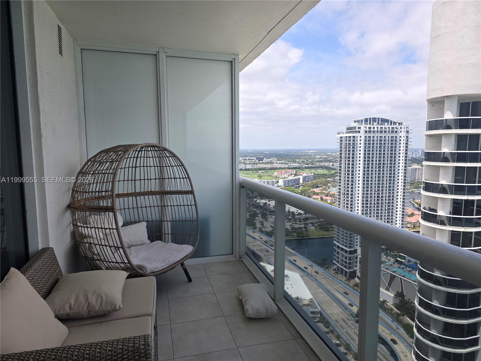 A high-rise balcony features a wicker egg chair, outdoor seating, and a city view — 1830 S Ocean Dr # 4309, Hallandale Beach FL 33009, HALLANDALE BEACH, FL