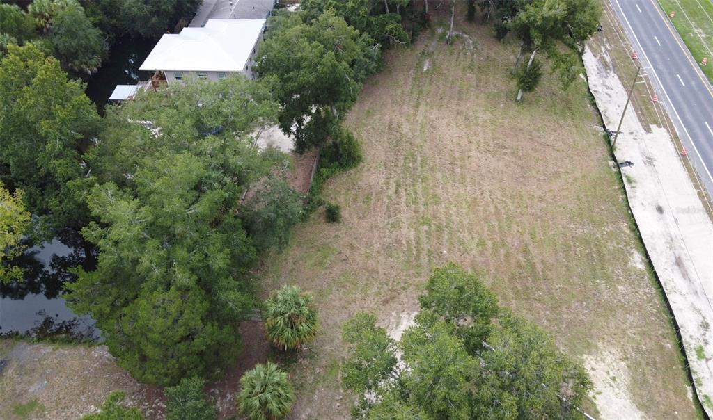 An aerial view shows a vacant, grassy lot bordered by trees, a road, and water — 8780 W KINGSTON DRIVE, HOMOSASSA, FL