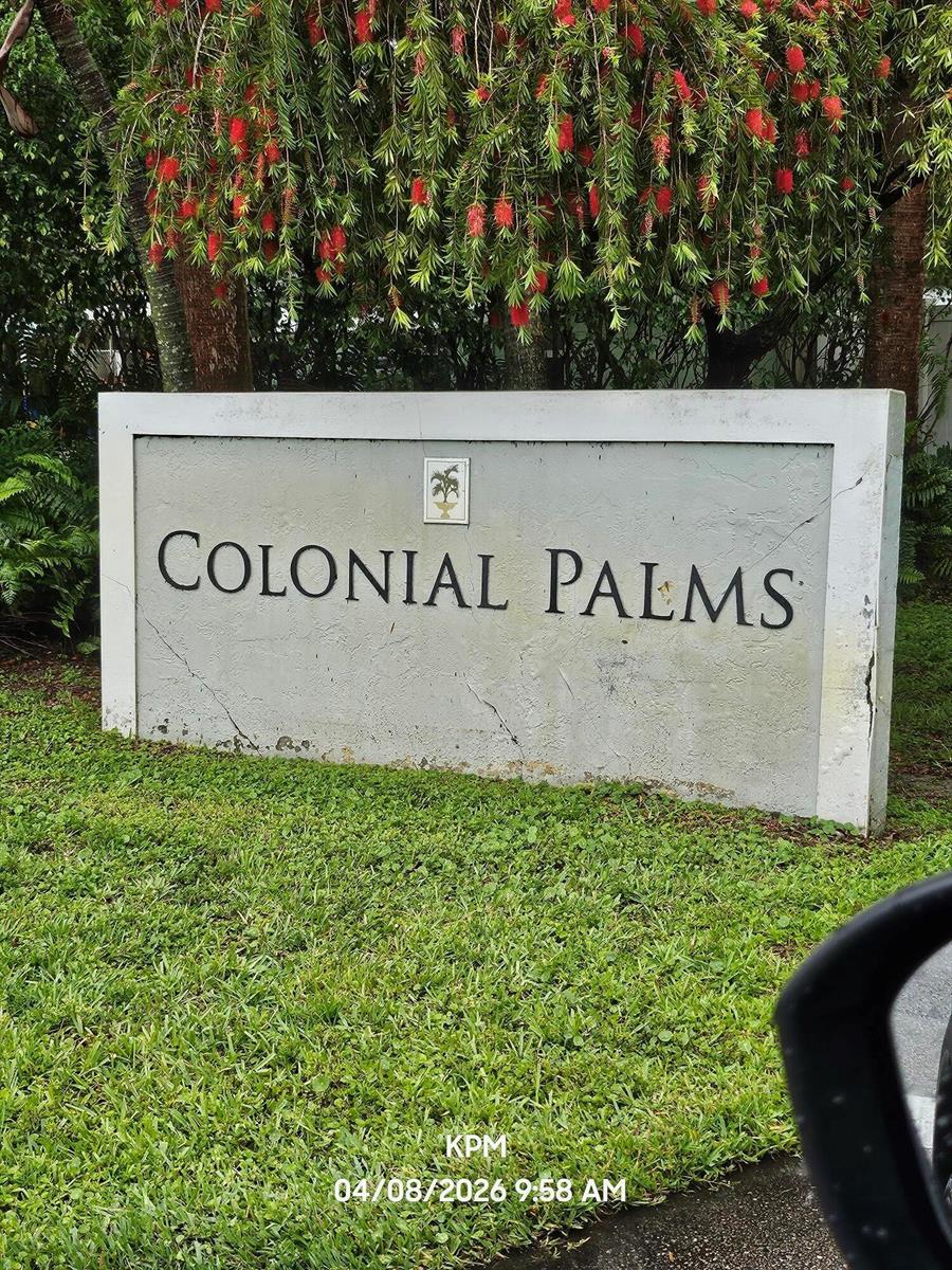 A concrete sign for Colonial Palms stands in a grassy area beneath a flowering tree — 1193 Colonial Palms Way, Palm Springs FL 33406, PALM SPRINGS, FL