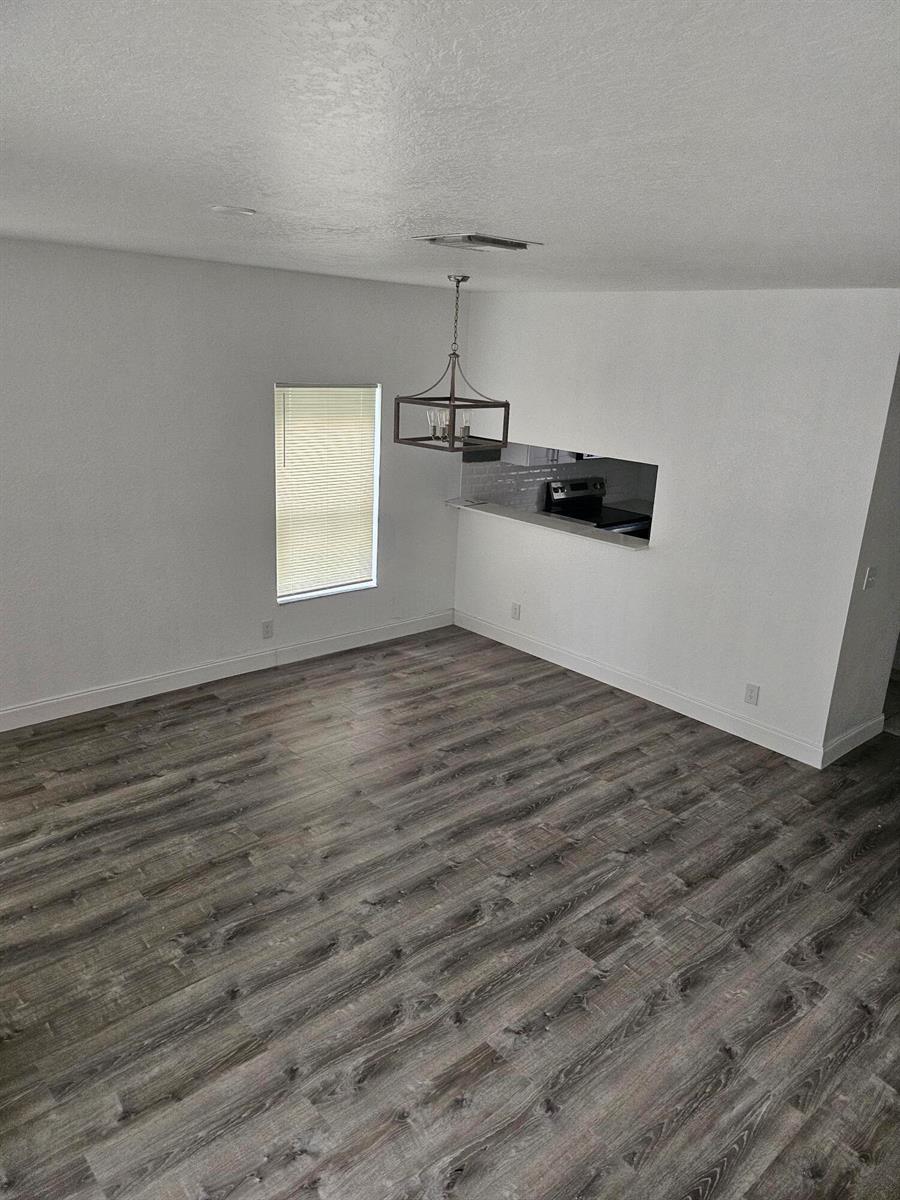 An empty dining area features wood-look flooring, a hanging light fixture, and a kitchen pass-through — 1193 Colonial Palms Way, Palm Springs FL 33406, PALM SPRINGS, FL