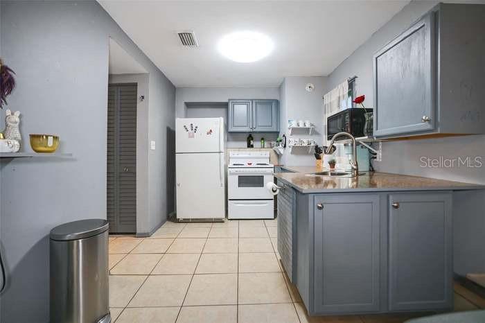 A kitchen features gray cabinets, a white stove, a white refrigerator, and light-colored tile flooring — 2650 25TH AVENUE N, ST PETERSBURG, FL