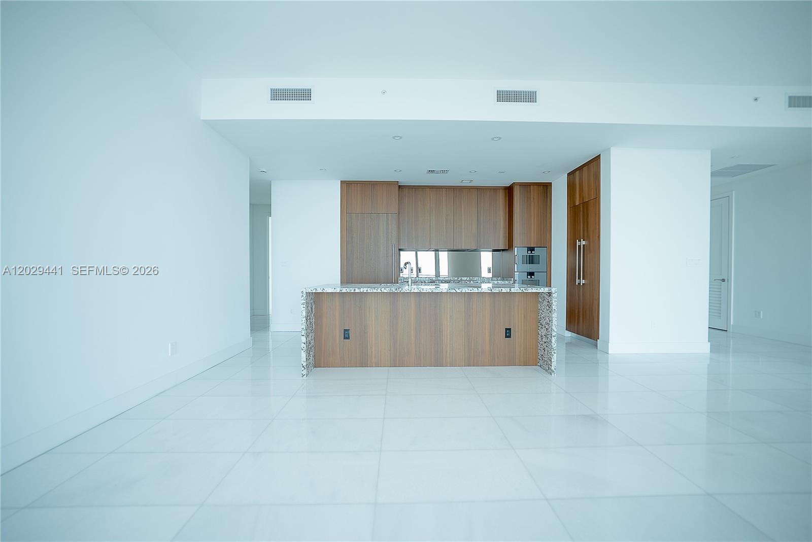 A modern kitchen features wood cabinetry, a granite-topped island, and white tile flooring — 175 SE 25th Rd # 2103, Miami FL 33129, MIAMI, FL