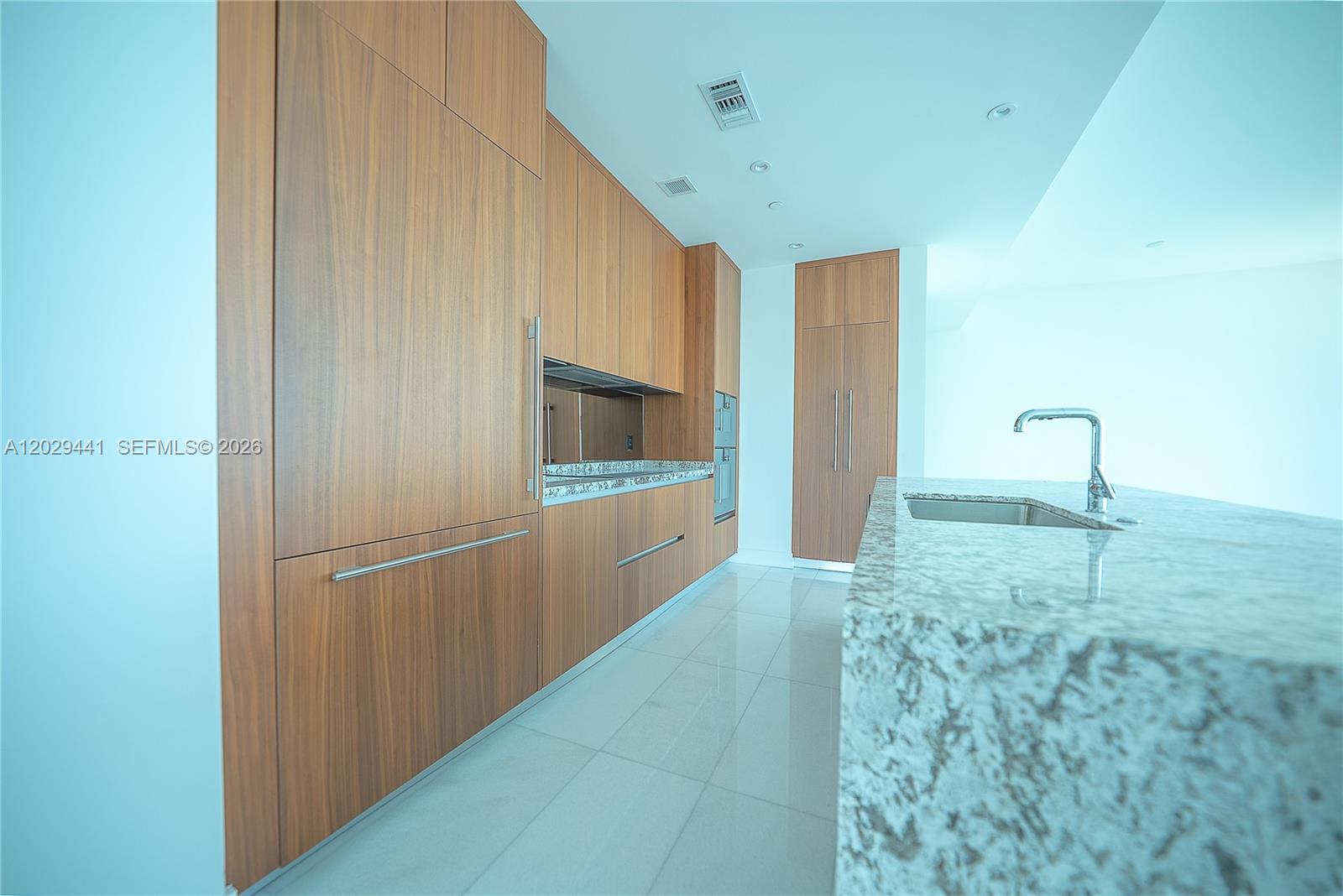 A modern kitchen features wood cabinetry, a granite island with a sink, and tile flooring — 175 SE 25th Rd # 2103, Miami FL 33129, MIAMI, FL