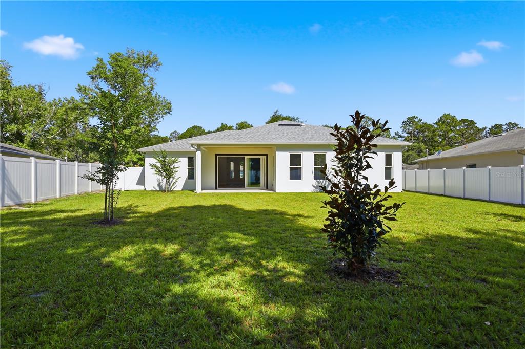The backyard of a single-story house features a lawn, white vinyl fencing, and young trees — 12 PERTHSHIRE LANE, PALM COAST, FL