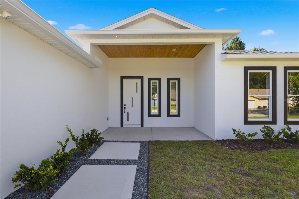 A modern white house exterior features a covered entryway with a wood-paneled ceiling — 12 PERTHSHIRE LANE, PALM COAST, FL