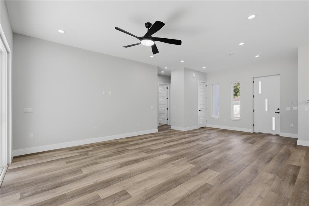 A bright, open-concept living room features light gray walls, wood-look flooring, and a ceiling fan — 12 PERTHSHIRE LANE, PALM COAST, FL