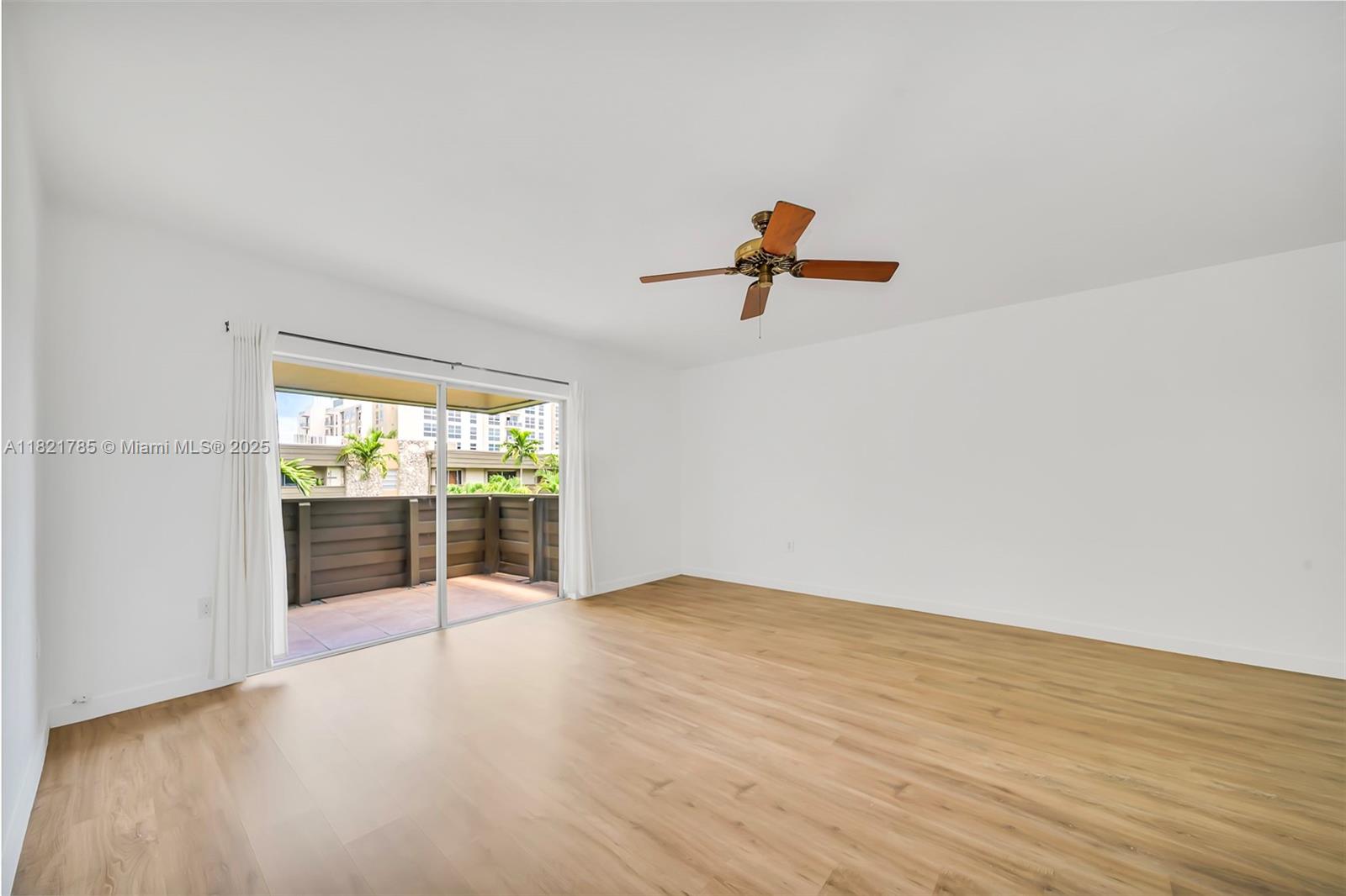 An empty room features light wood-look flooring, white walls, a ceiling fan, and a sliding glass door — 8335 SW 72nd Ave # 315D, Miami FL 33143, MIAMI, FL