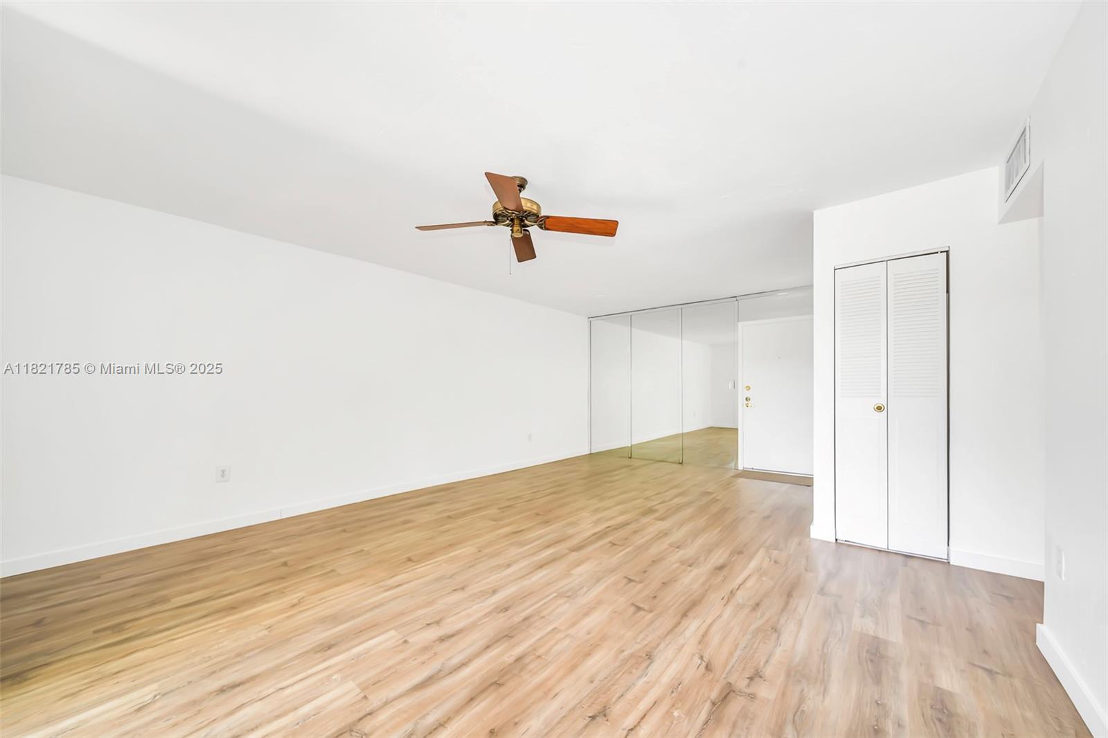 An empty room features light wood-look flooring, white walls, a ceiling fan, and mirrored closet doors — 8335 SW 72nd Ave # 315D, Miami FL 33143, MIAMI, FL