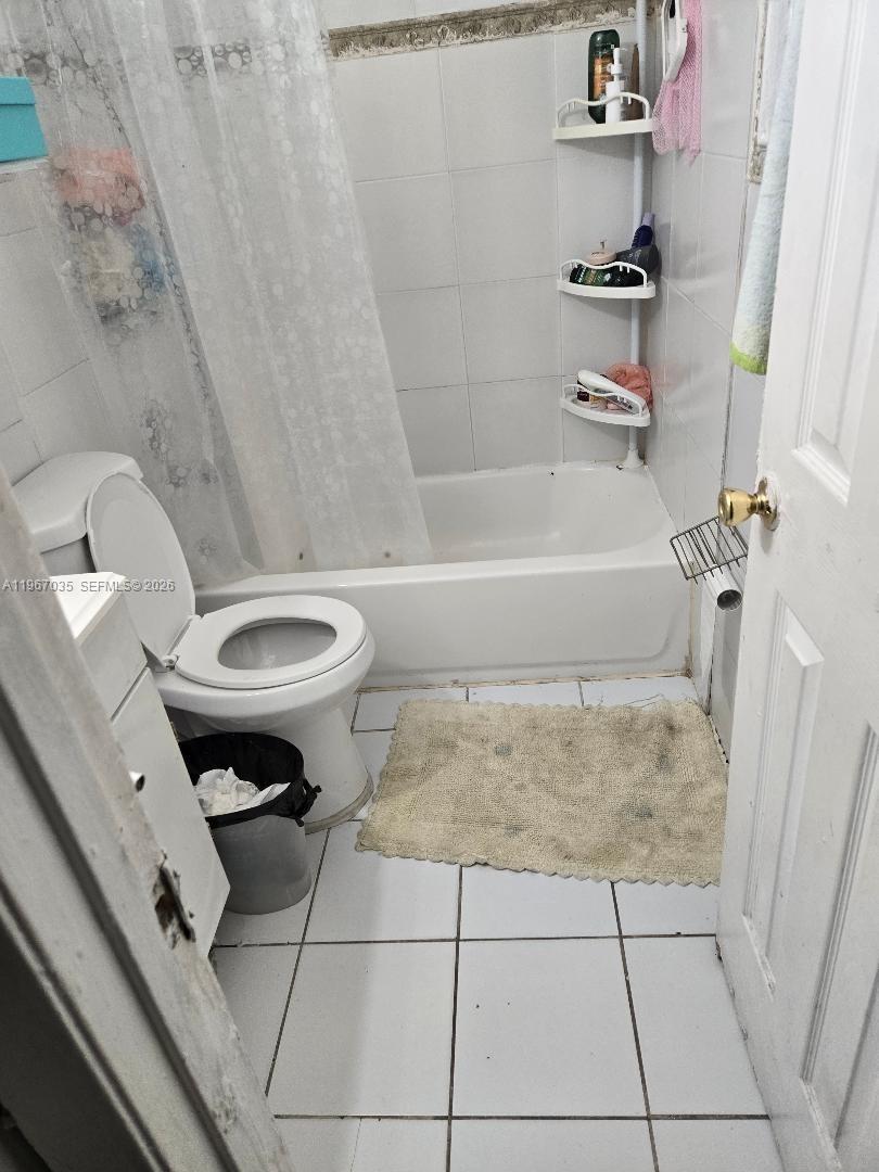 A small bathroom features a white toilet, a bathtub with a shower curtain, and tile flooring — 2100 NW 4th St, Pompano Beach FL 33069, POMPANO BEACH, FL