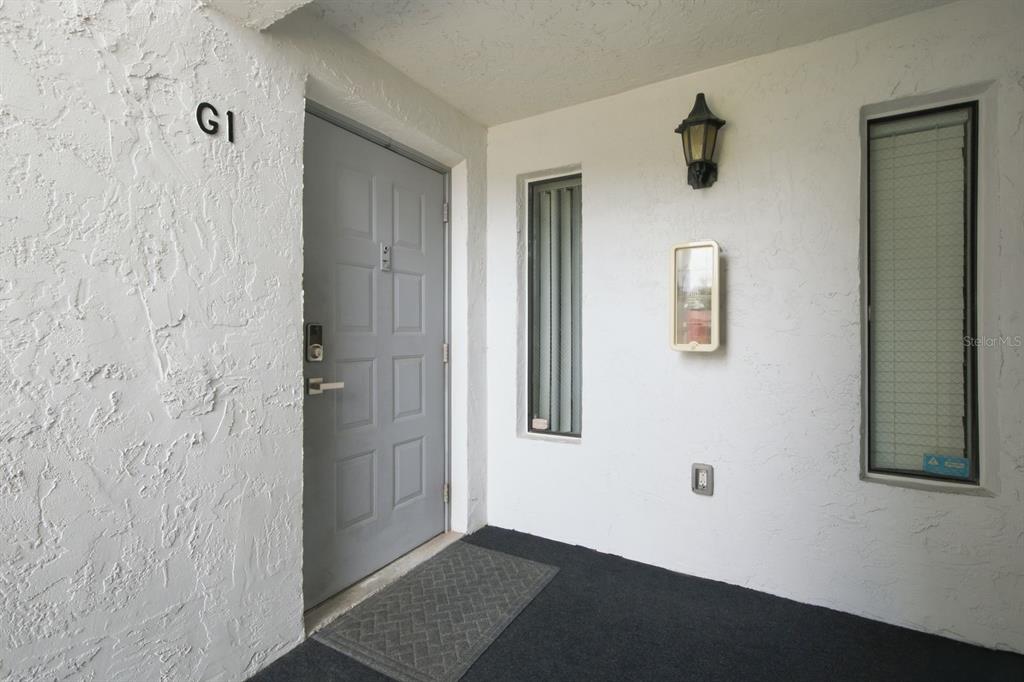 A gray front door with a keypad lock sits under a light fixture — 1179 PINE RIDGE CIRCLE W UNIT G1, TARPON SPRINGS, FL