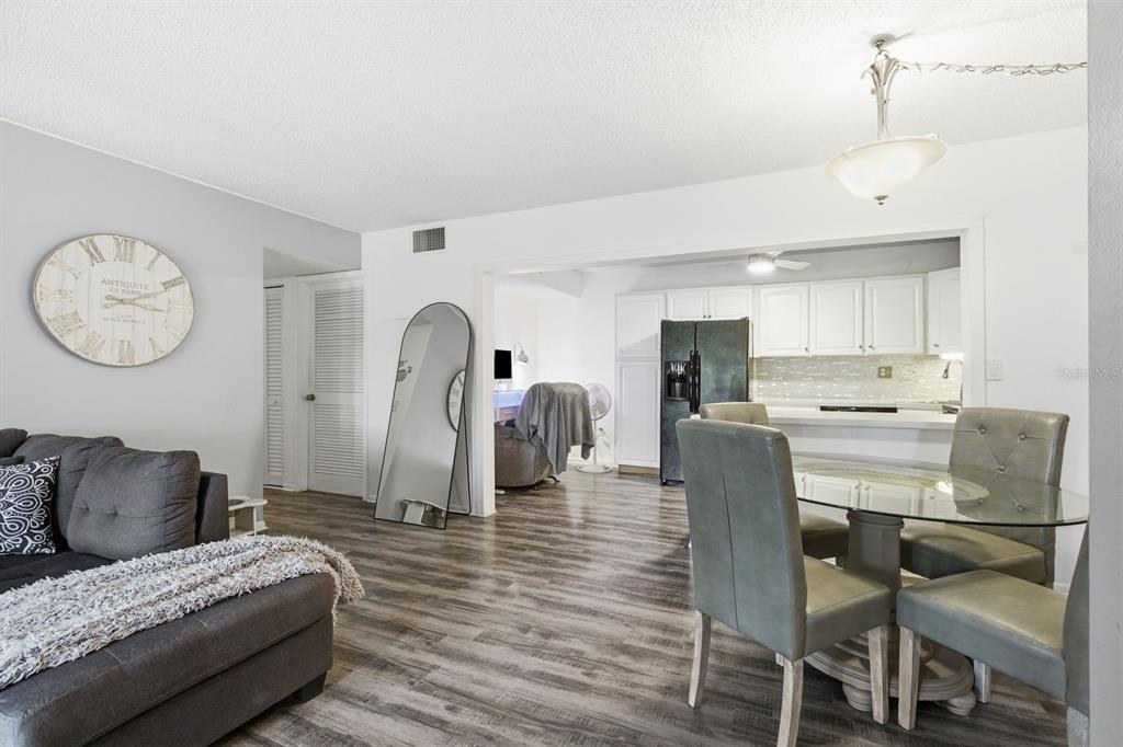 A living room with wood-look flooring flows into a dining area and an open kitchen — 1179 PINE RIDGE CIRCLE W UNIT G1, TARPON SPRINGS, FL