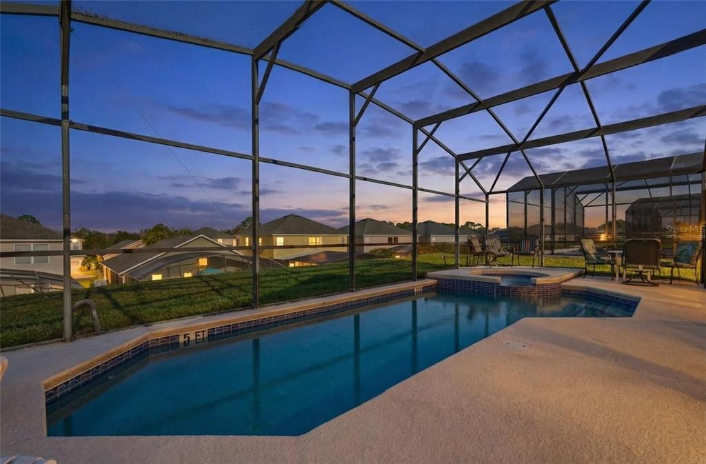 A screened-in swimming pool and spa at dusk with a view of neighboring houses — 8595 SUNRISE KEY DRIVE, KISSIMMEE, FL