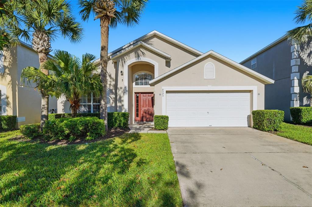 A beige single-story house with a two-car garage, arched entryway, and palm trees — 8595 SUNRISE KEY DRIVE, KISSIMMEE, FL