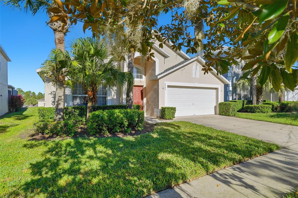 A beige single-story house with a white garage door, palm trees, and a green lawn — 8595 SUNRISE KEY DRIVE, KISSIMMEE, FL