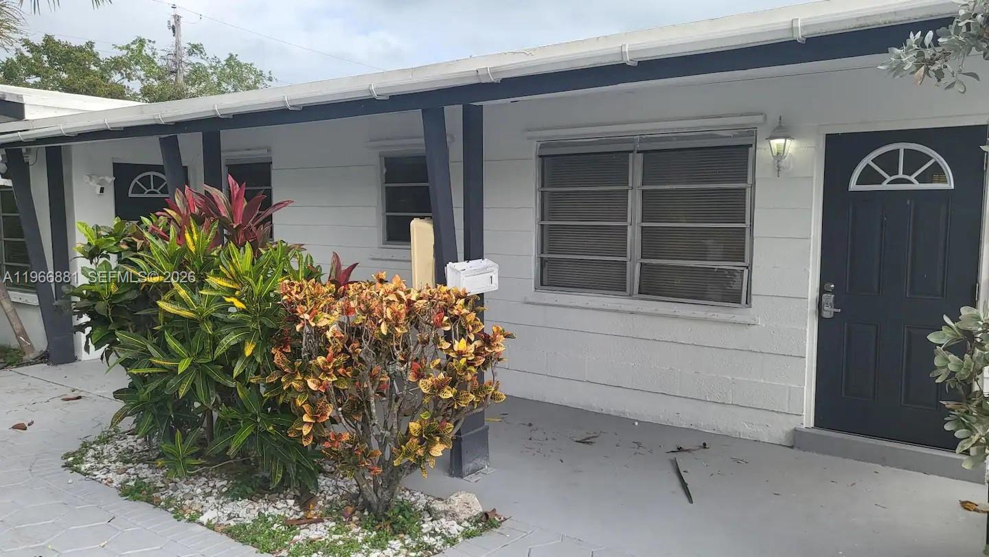 A white exterior wall with a dark door, a window, and a small garden area — 821 NE 6th St # 1, Hallandale Beach FL 33009, HALLANDALE BEACH, FL
