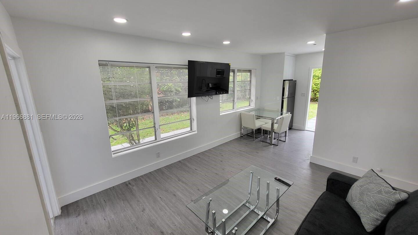 A living area features gray wood-look flooring, a wall-mounted television, and a small dining set — 821 NE 6th St # 1, Hallandale Beach FL 33009, HALLANDALE BEACH, FL