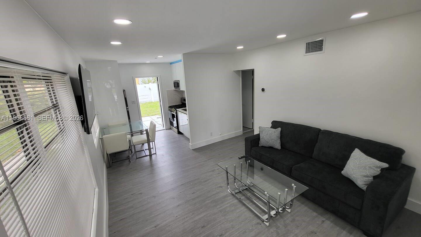 A living room with gray flooring, a dark sofa, and an adjacent kitchen area — 821 NE 6th St # 1, Hallandale Beach FL 33009, HALLANDALE BEACH, FL