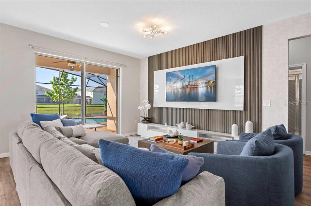 A living room features a slatted wood accent wall, a television, and sliding glass doors — 4443 SHIVA LOOP, KISSIMMEE, FL