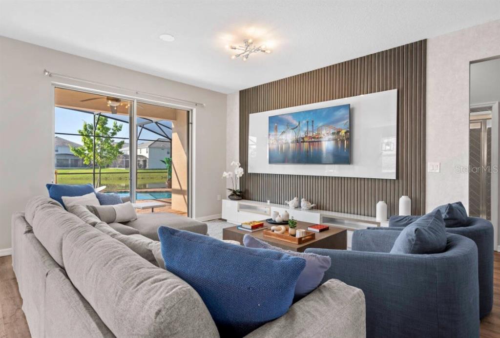 A living room features a slatted wood accent wall, a mounted television, and sliding glass doors — 4443 SHIVA LOOP, KISSIMMEE, FL