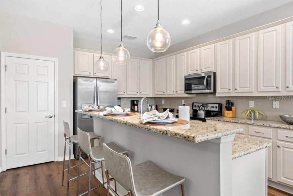 A kitchen features white cabinets, granite countertops, a breakfast bar with stools, and pendant lighting — 4443 SHIVA LOOP, KISSIMMEE, FL