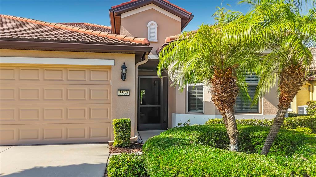 A tan house exterior features a two-car garage, a front entryway, and palm trees — 5539 SUNSET FALLS DRIVE, APOLLO BEACH, FL