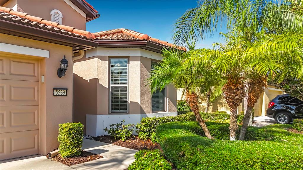 A beige house exterior features a garage, a bay window, and palm trees — 5539 SUNSET FALLS DRIVE, APOLLO BEACH, FL