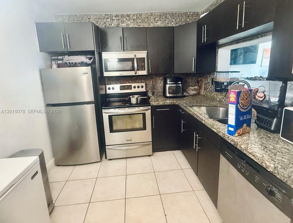 A kitchen features dark cabinetry, stainless steel appliances, granite countertops, and a tiled backsplash — 488 NW 165th St Rd # 512, Miami FL 33169, MIAMI, FL