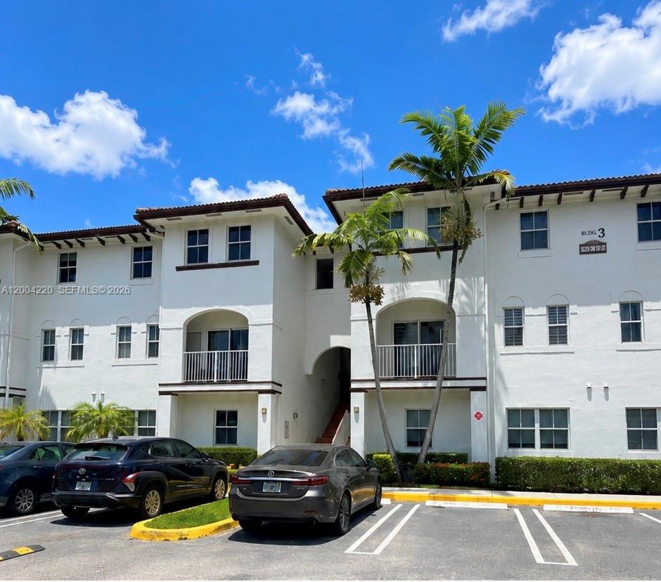 A two-story white stucco apartment building with a parking lot in the foreground — 8900 NW 97th Ave # 104, Doral FL 33178, DORAL, FL