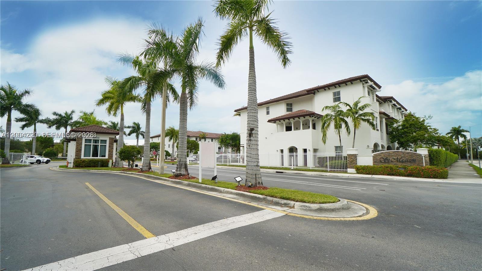 A gated entrance features palm trees, a guardhouse, and a multi-story white building — 8900 NW 97th Ave # 104, Doral FL 33178, DORAL, FL