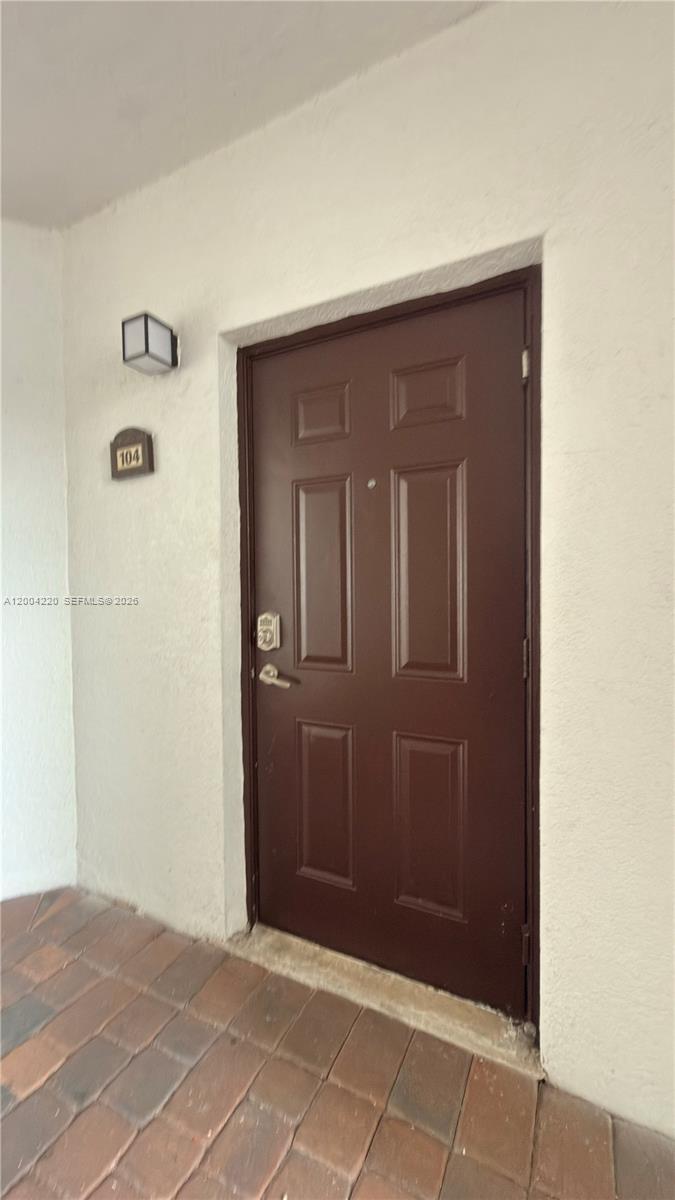 A brown front door with a number 104 sign is set against a white wall — 8900 NW 97th Ave # 104, Doral FL 33178, DORAL, FL