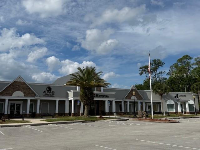 A commercial building with a parking lot and a palm tree under a cloudy sky — 20 AIRPORT ROAD UNIT D&E, PALM COAST, FL