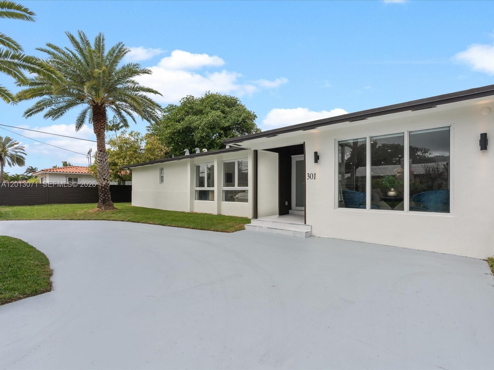 A white single-story house features a large gray driveway, a palm tree, and large windows — 301 88th St, Surfside FL 33154, SURFSIDE, FL