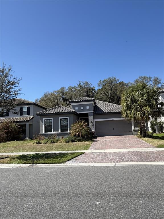A single-story gray house with a tiled roof and a brick driveway under a clear sky — 3818 ROSE MALLOW DRIVE, KISSIMMEE, FL