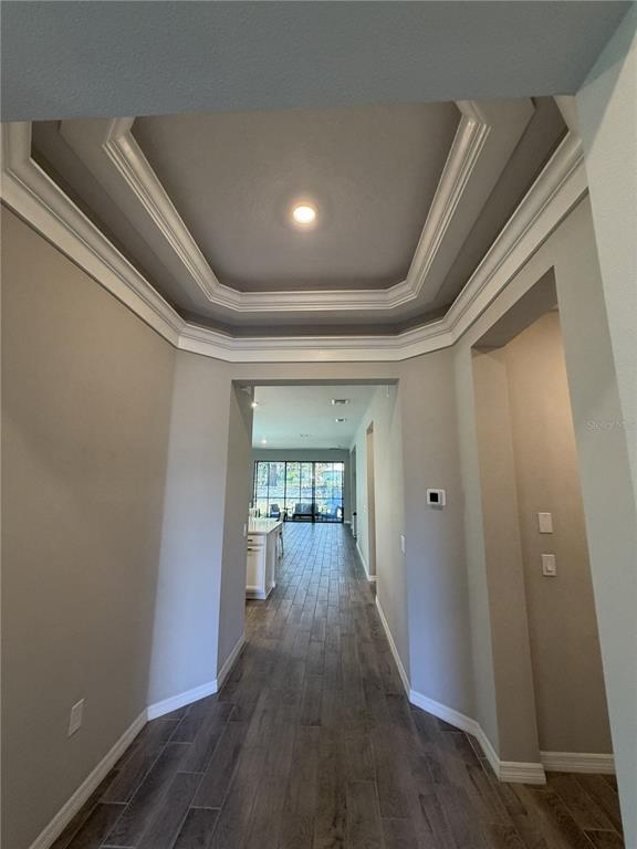 A hallway with a tray ceiling leads to an open-concept living area with tile flooring — 3818 ROSE MALLOW DRIVE, KISSIMMEE, FL