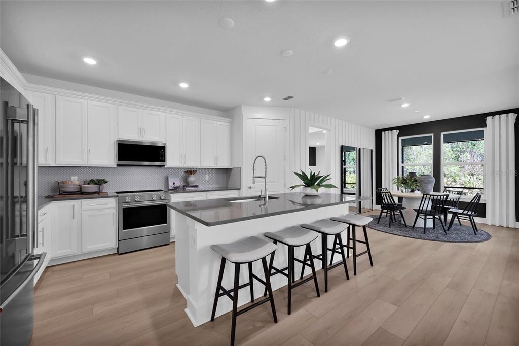 A modern kitchen features white cabinetry, a gray island with bar stools, and a dining area — 308 FISHTAIL PLACE, PALM COAST, FL