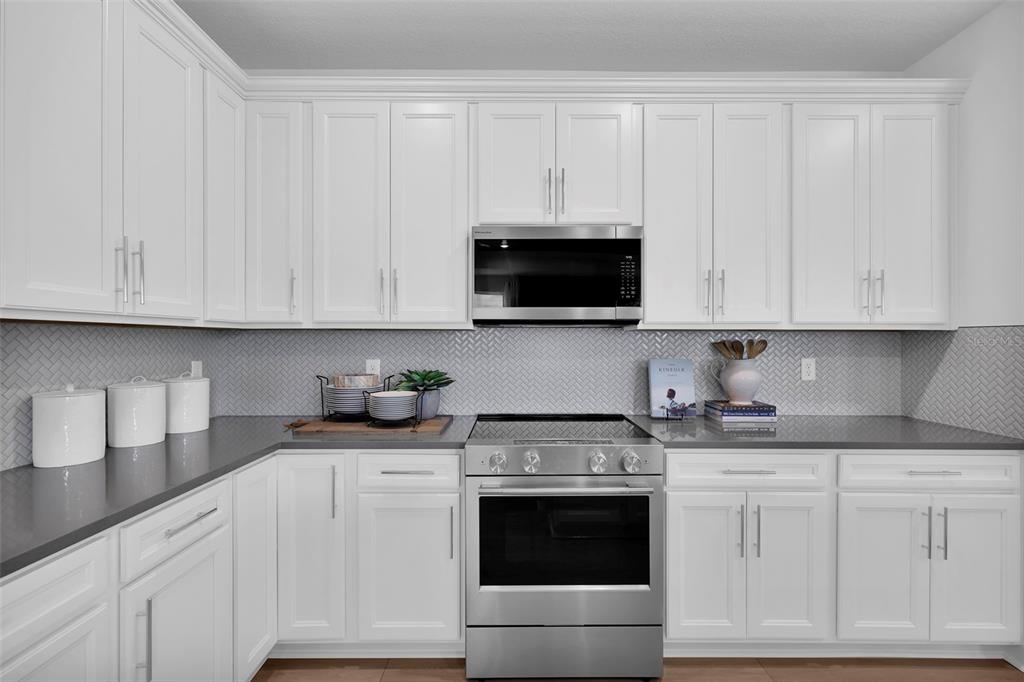 A kitchen with white cabinets, stainless steel appliances, gray countertops, and a herringbone tile backsplash — 308 FISHTAIL PLACE, PALM COAST, FL
