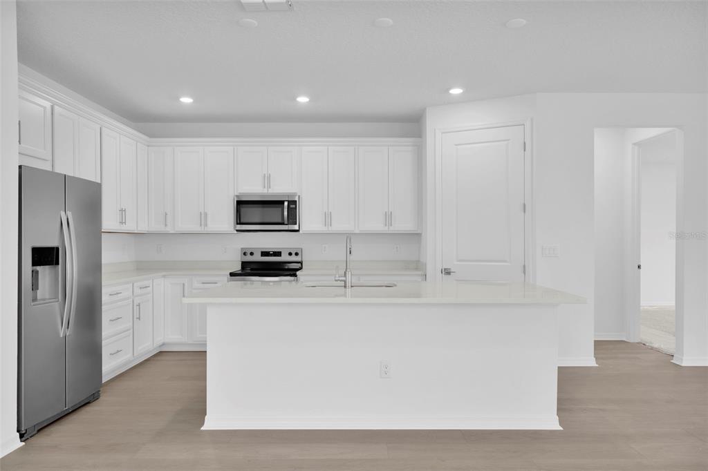 A modern kitchen features white cabinets, stainless steel appliances, a center island, and light flooring — 308 FISHTAIL PLACE, PALM COAST, FL