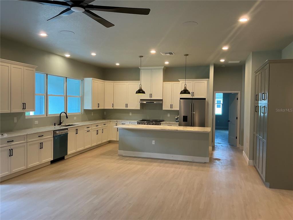 A modern kitchen features white cabinetry, a central island, stainless steel appliances, and light flooring — 1619 MAGNOLIA AVENUE, DELAND, FL