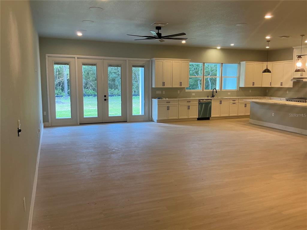 An open-concept kitchen and living area features light wood flooring, white cabinetry, and glass doors — 1619 MAGNOLIA AVENUE, DELAND, FL