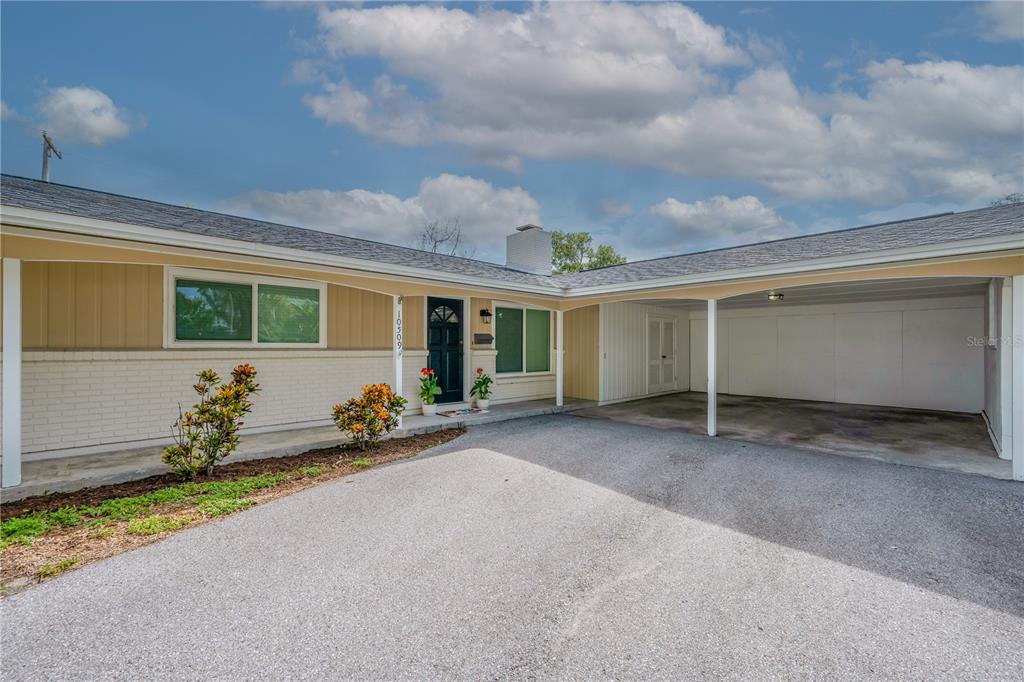 A single-story house exterior features a beige facade, a dark front door, and a carport — 10509 ORANGE GROVE DRIVE, TAMPA, FL