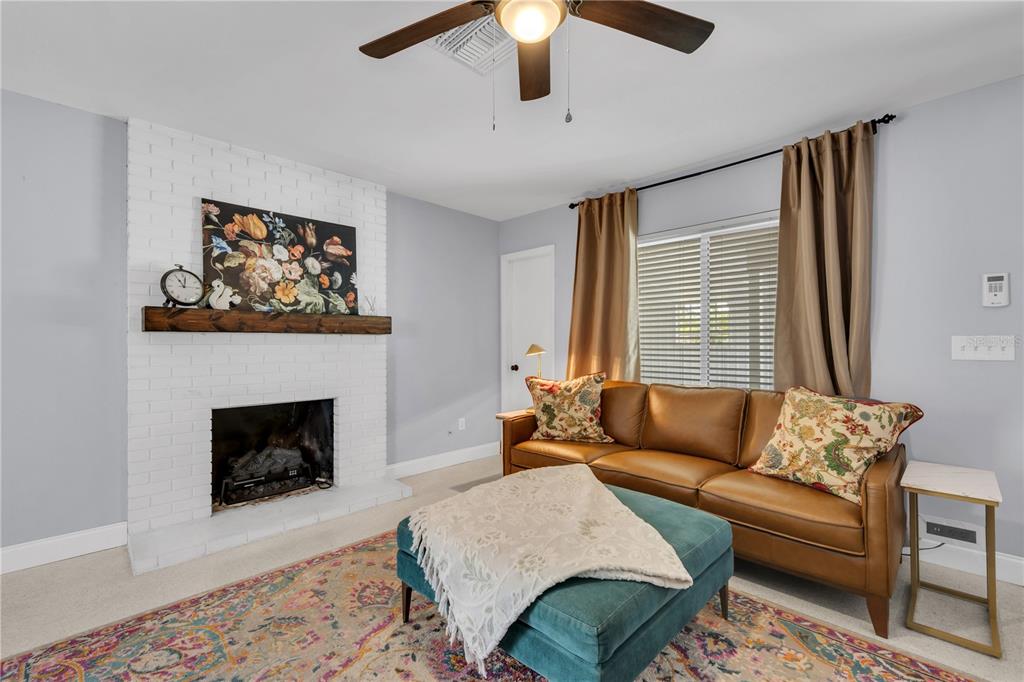A living room features a white brick fireplace, leather sofas, a teal ottoman, and carpet — 10509 ORANGE GROVE DRIVE, TAMPA, FL